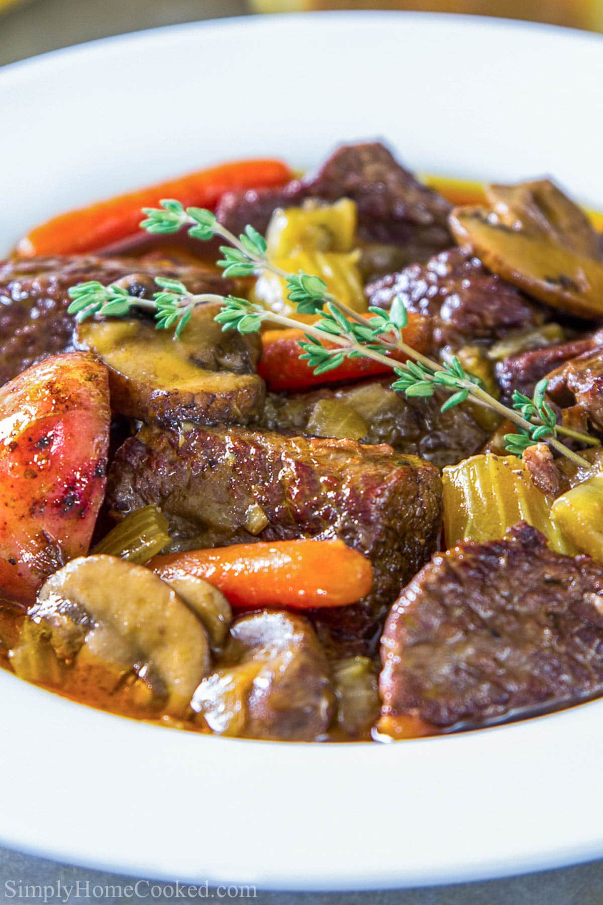 Closeup of Beef Stew in a bowl with a sprig of rosemary on top.