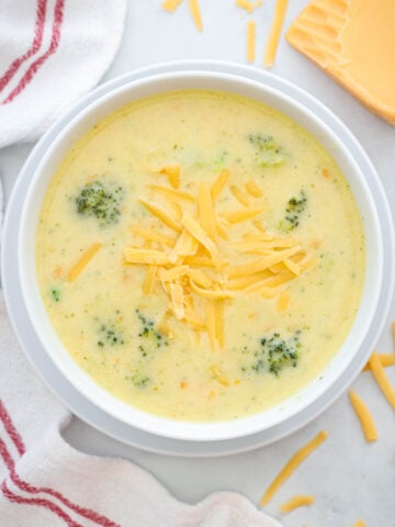 Overhead view of a bowl of Broccoli Cheddar Soup with shredded cheese on top.