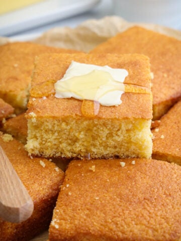 Stack of Buttermilk Cornbread squares with a pat of butter melting on one with honey.