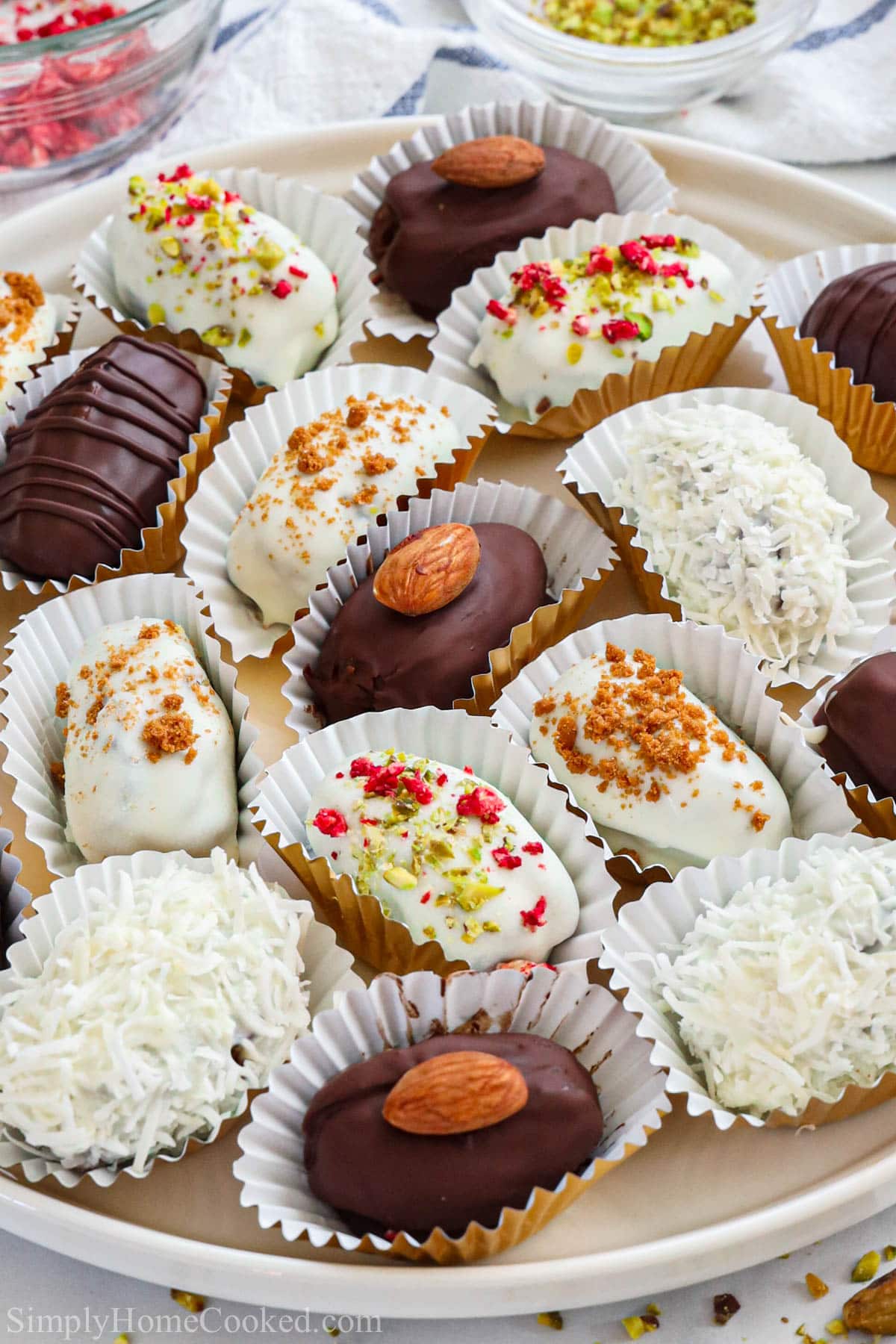 Plate of Chocolate Covered Dates in wrappers, some topped with nuts and coconut flakes.