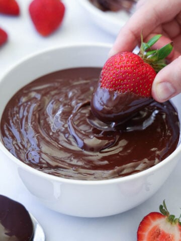 Hand dipping a strawberry into a bowl of Chocolate Ganache