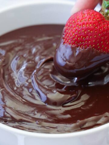 Hand dipping a strawberry into a bowl of Chocolate Ganache