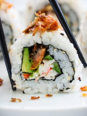 Salmon Skin Roll cut and topped with crispy salmon skins being picked up by chopsticks.