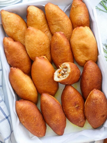 Piroshki lined up in a container with one missing a bite