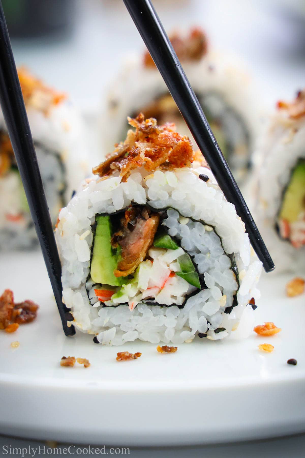 Salmon Skin Roll cut and topped with crispy salmon skins being picked up by chopsticks.