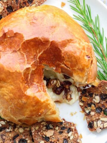Baked Brie in Puff Pastry on a white plate with rosemary sprigs and bread slices.