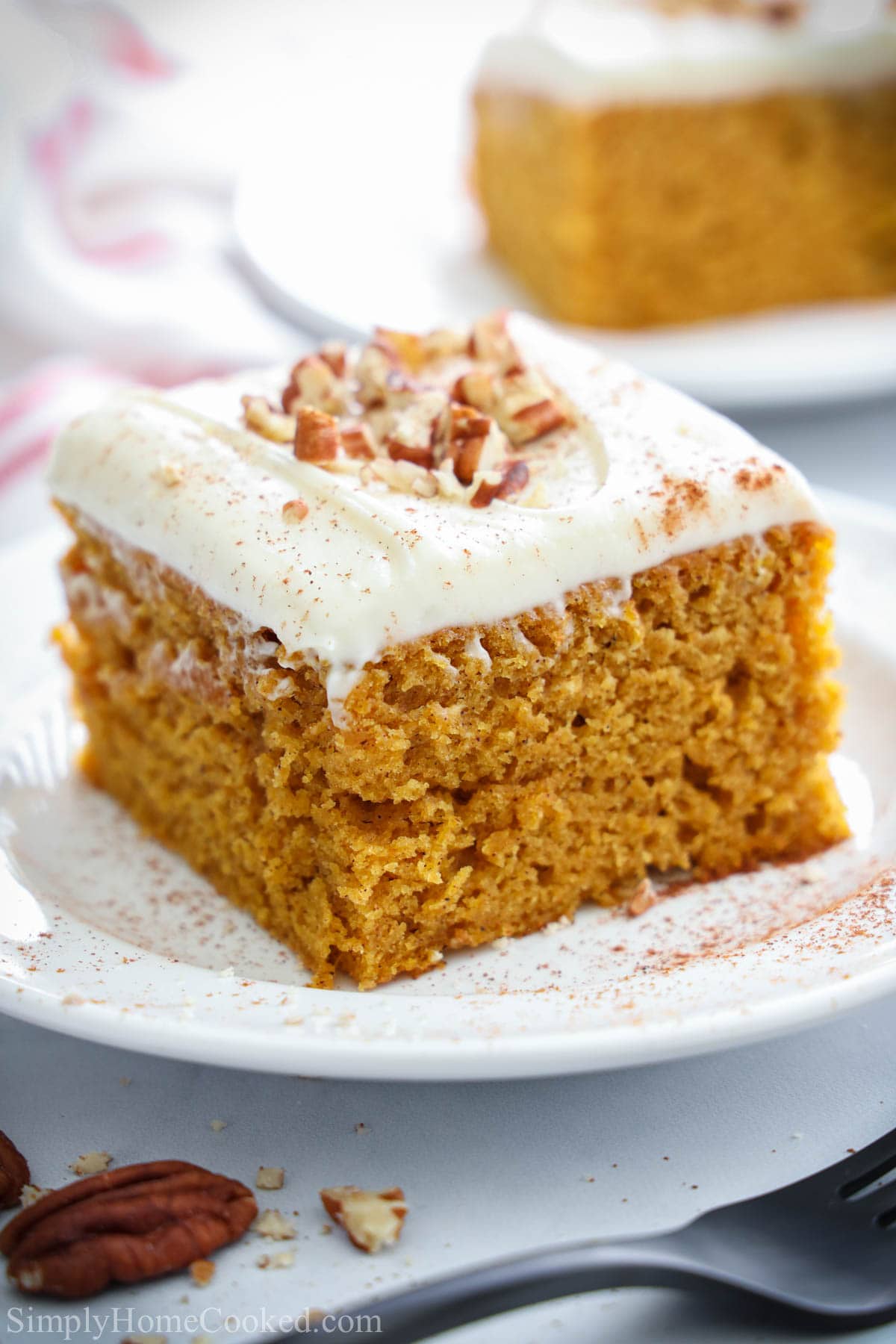 Slice of Pumpkin Cake on a white plate with pecans on top of the cream cheese frosting.