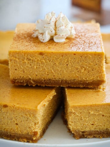 Pumpkin Cheesecke Bars stacked up adn topped with whipped cream.