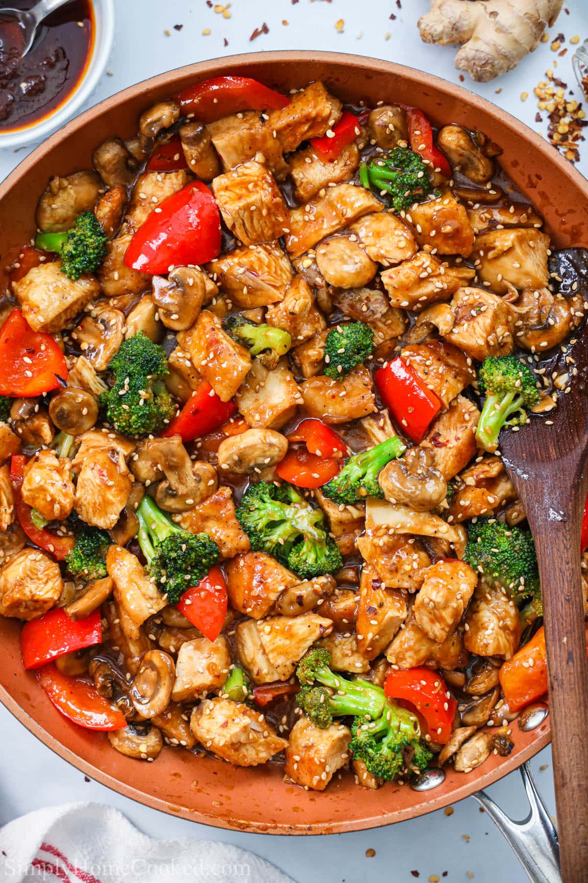 Skillet of Hunan Chicken and vegetables with a wooden spoon stirring