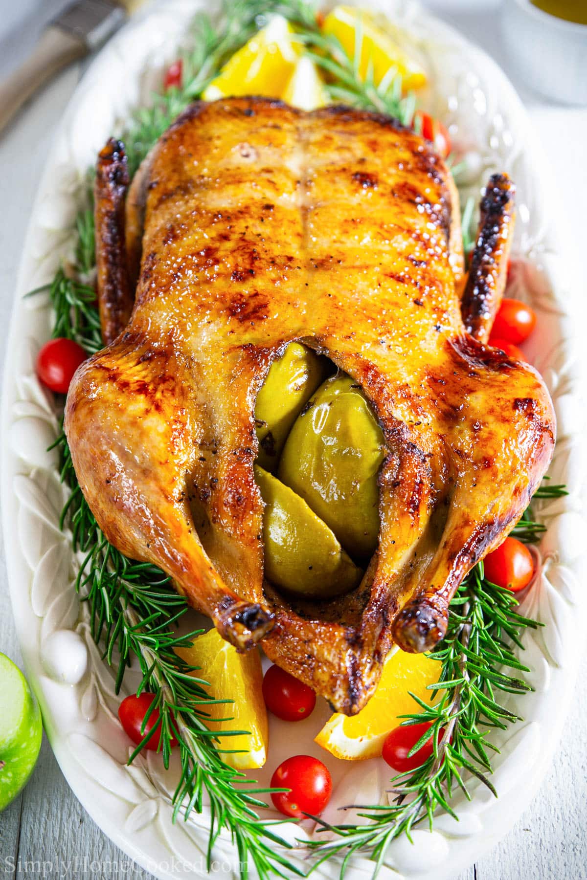 Roast Duck stuffed with apples and surrounded by rosemary, tomatoes, and oranges.