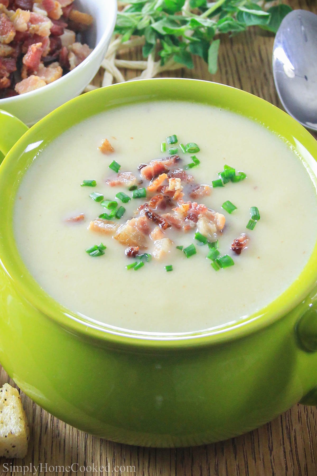 Potato Leek Soup topped with bacon and chives in a green bowl.