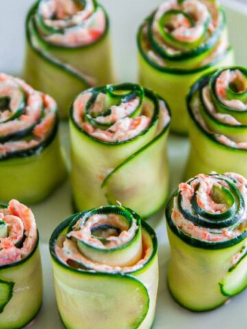 Plate of Smoked Salmon Appetizers made with rolled cucumber slices, salmon, cream cheese, and dill.