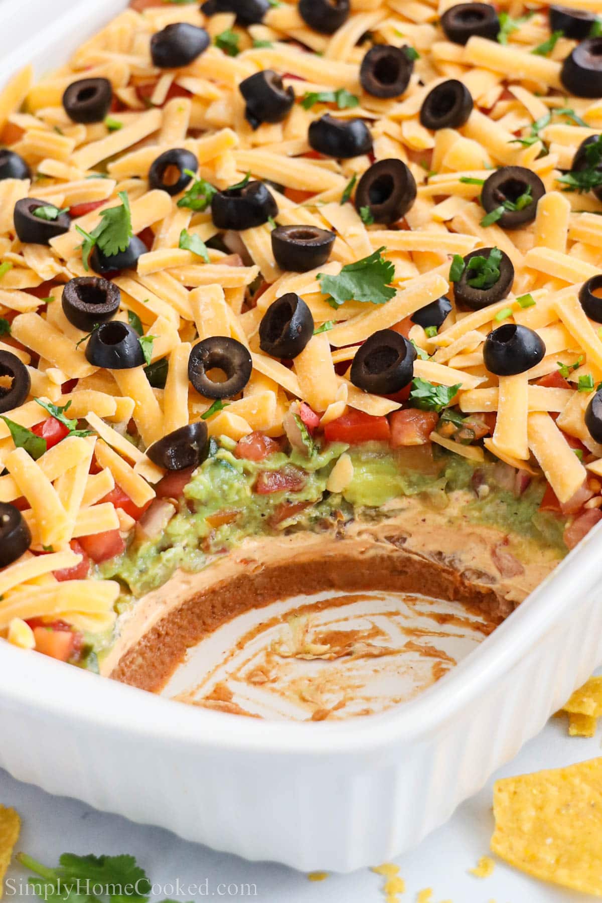 This 7-layer dip is layered with guacamole, pico de gallo, beans, sour cream, and olives. It's such a crowd puller! Perfect for parties or game day! #7layerdip #gamedayfood #mexicanapetizer #layereddip #diprecipe Baking pan with 7-layer taco dip missing a ball.