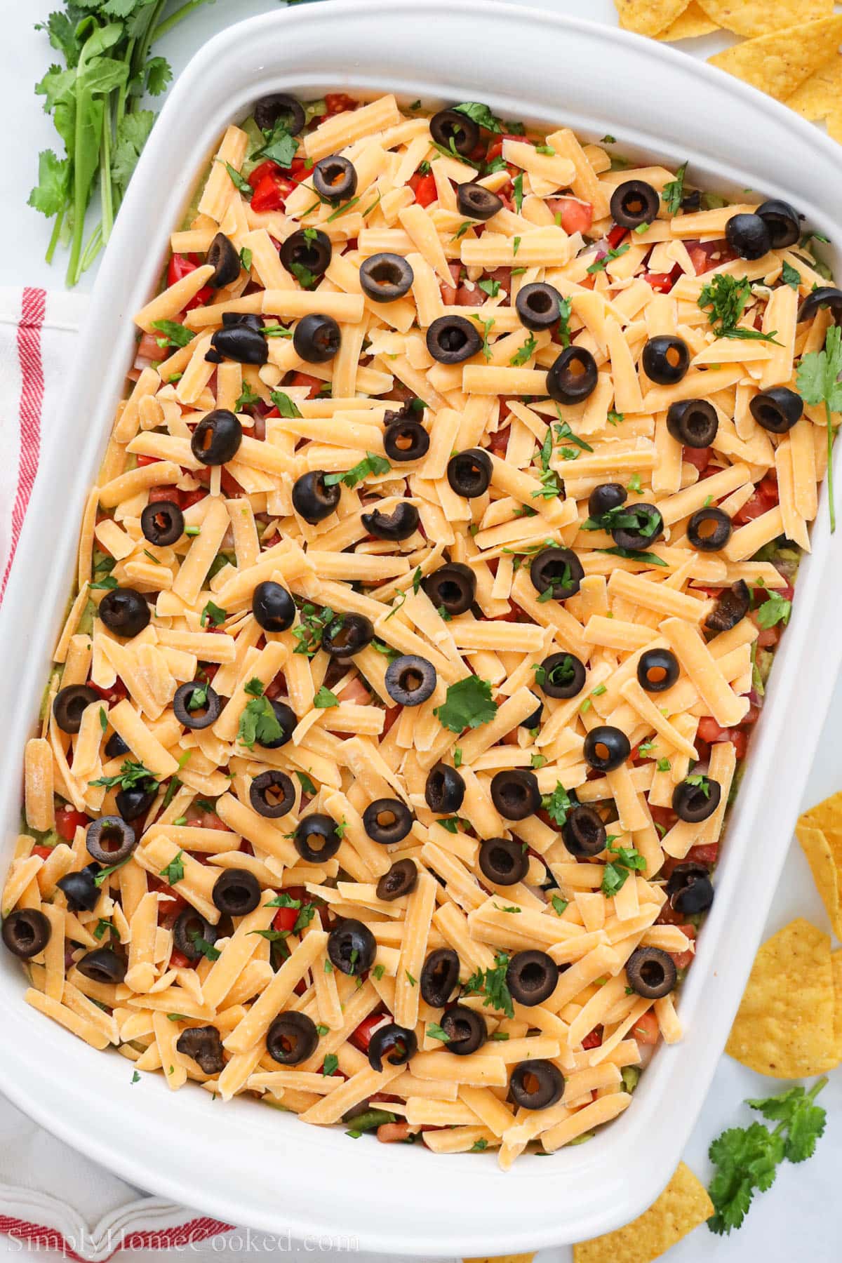 Casserole dish with 7-layer taco dip, topped with cilantro and black olives.