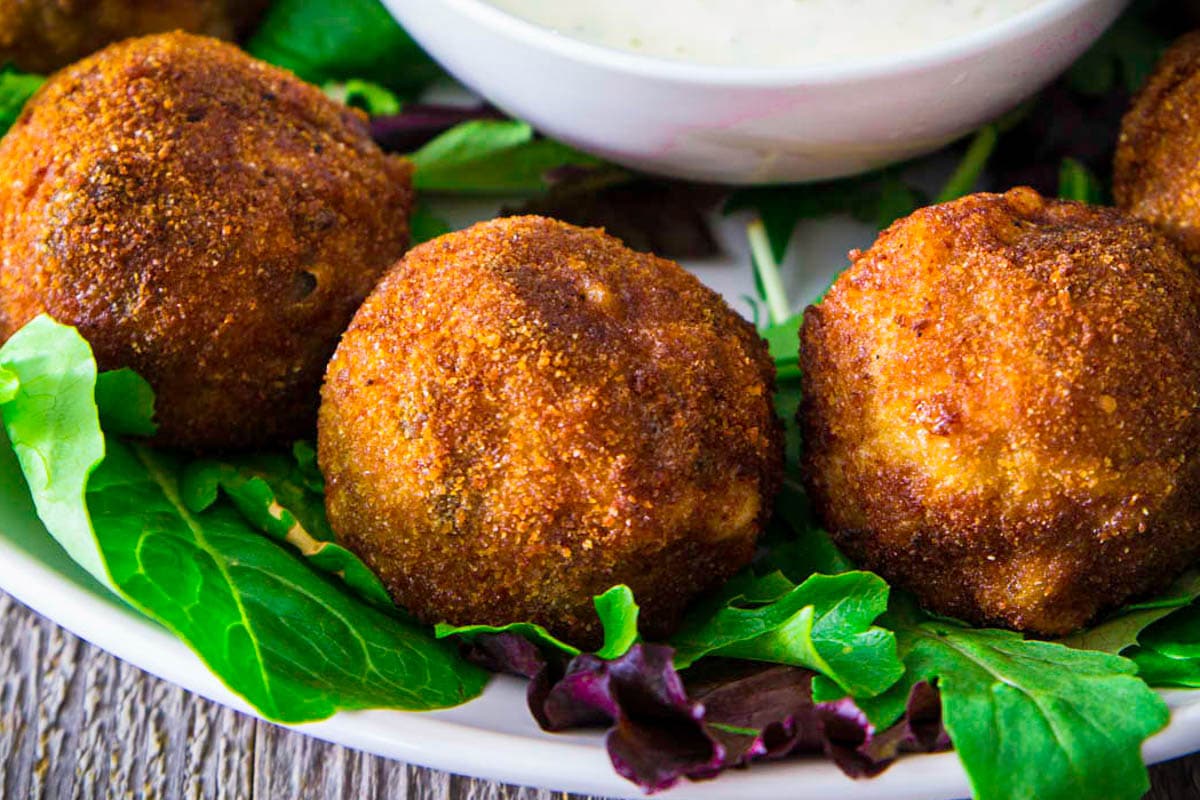 Chicken croquettes on a bed of lettuce near a bowl of ranch dressing.