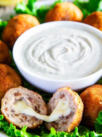 Chicken Croquettes around a bowl of ranch dressing, one split in half to show the gooey cheese.
