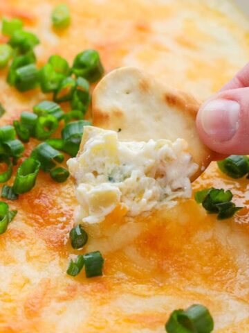 Crab Artichoke Dip topped with green onions and a chip being dipped into it.