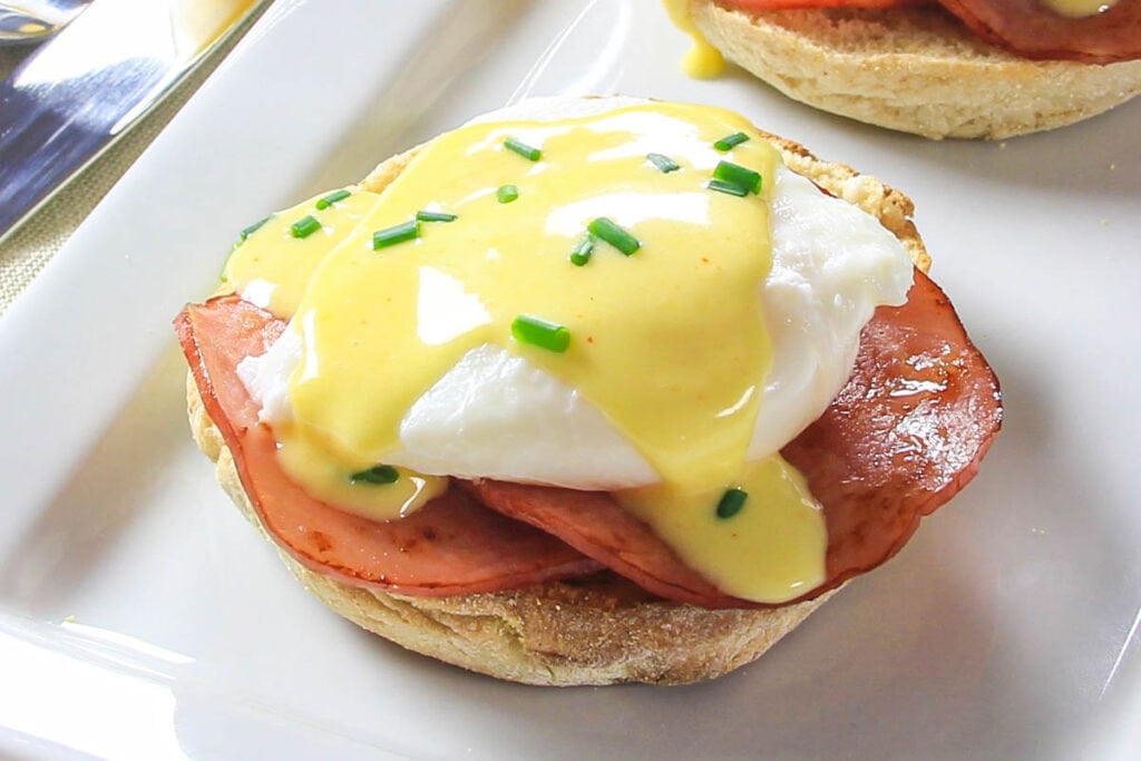 Eggs Benedict on an English muffin with Canadian bacon, egg, and hollandaise sauce on top.