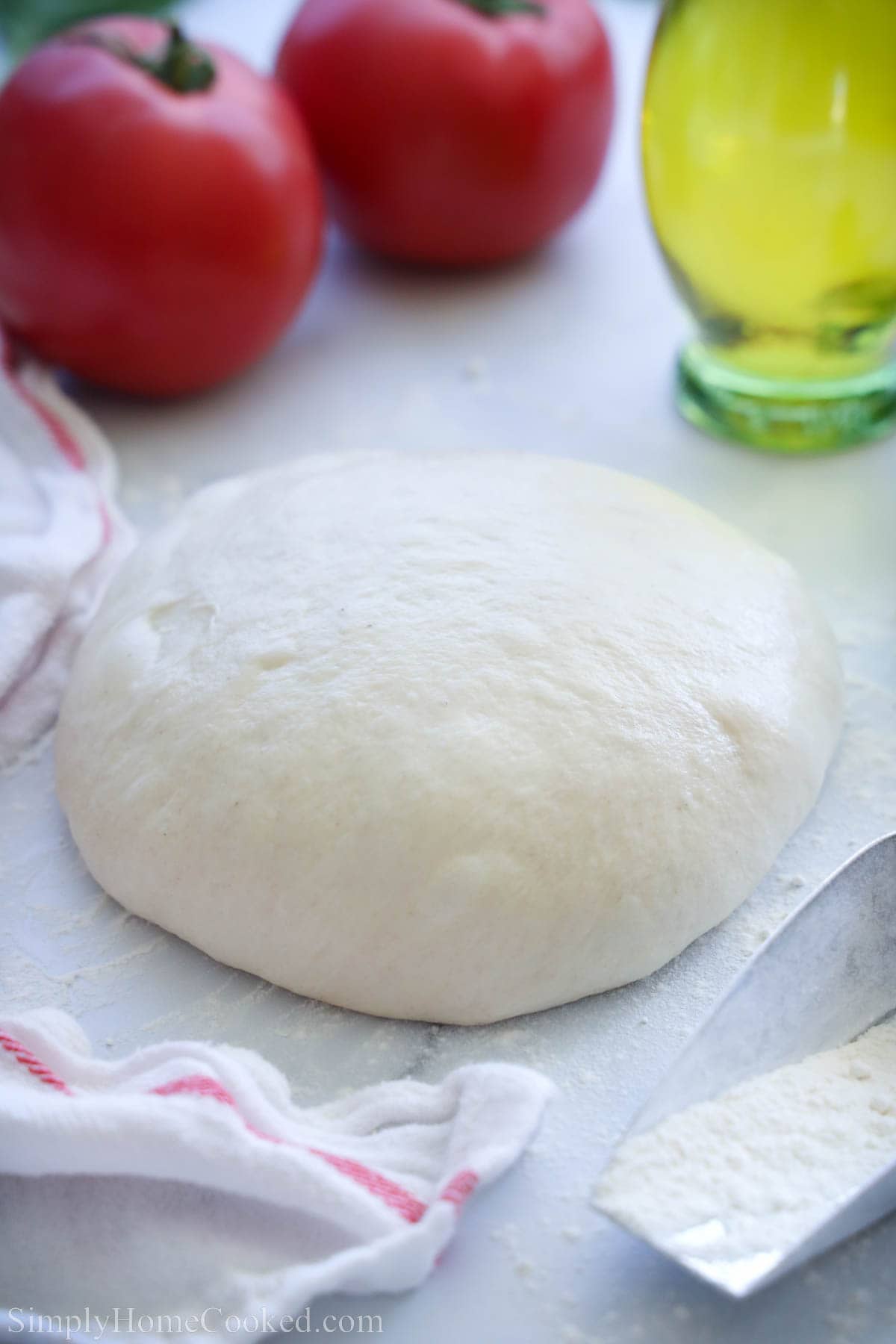 Homemade pizza dough near tomatoes and olive oil.
