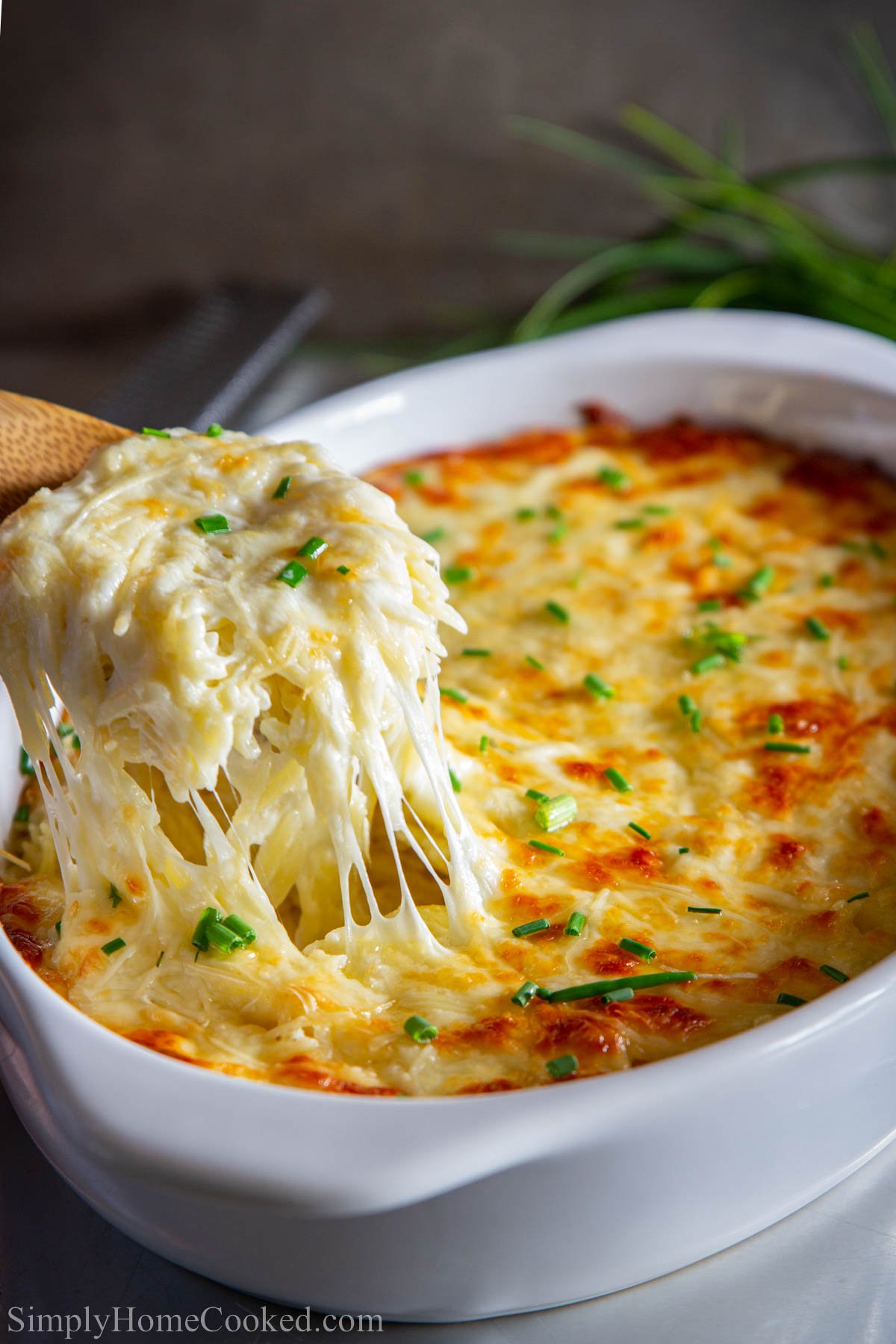 Baking dish of Creamy Orzo sprinkled with chopped chives, a spoonful being lifted out.