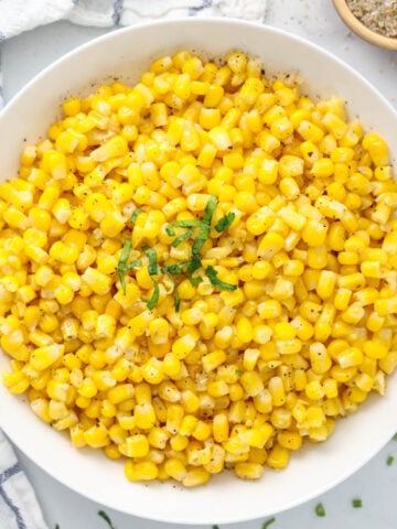A bowl of Corn topped with chopped parsley.