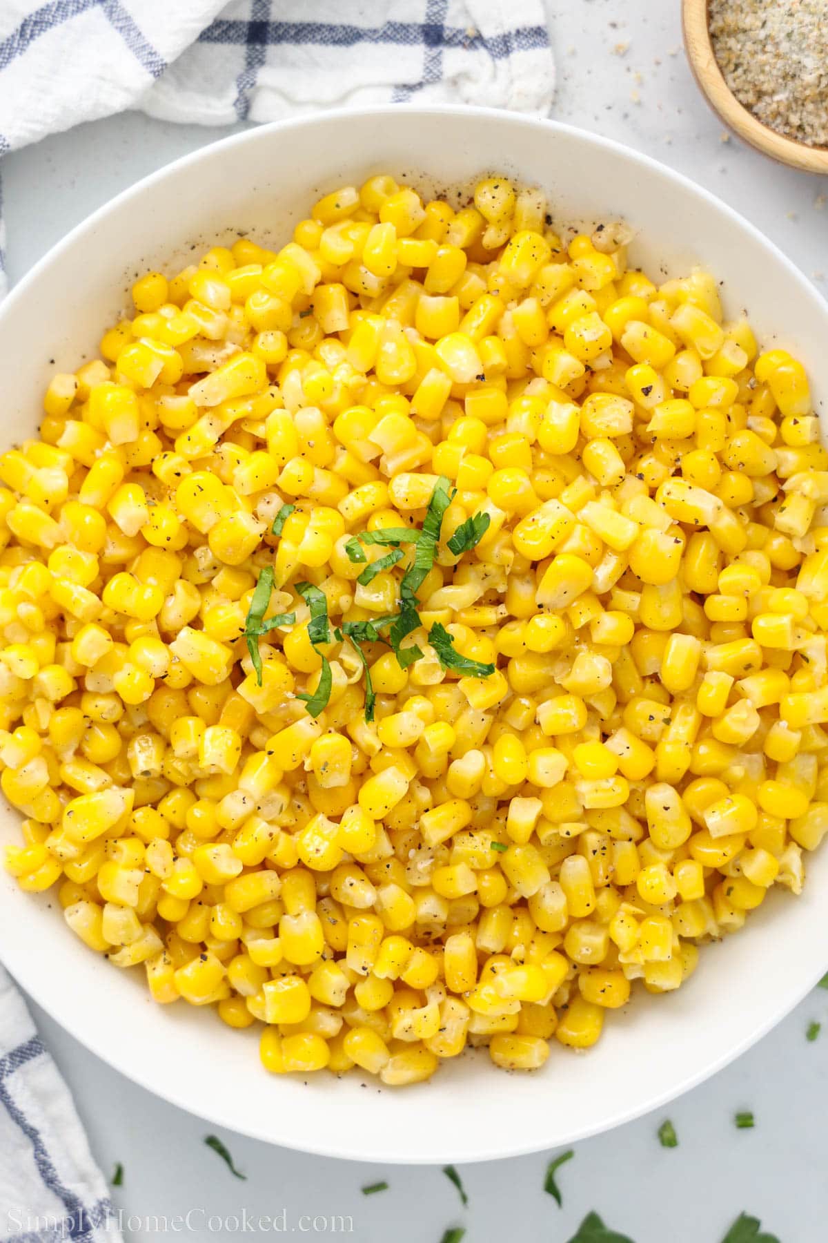 A bowl of Corn topped with chopped parsley.
