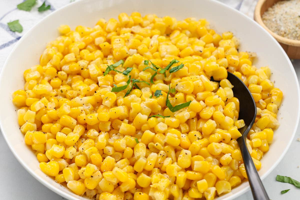 A bowl of corn with a spoon in it.