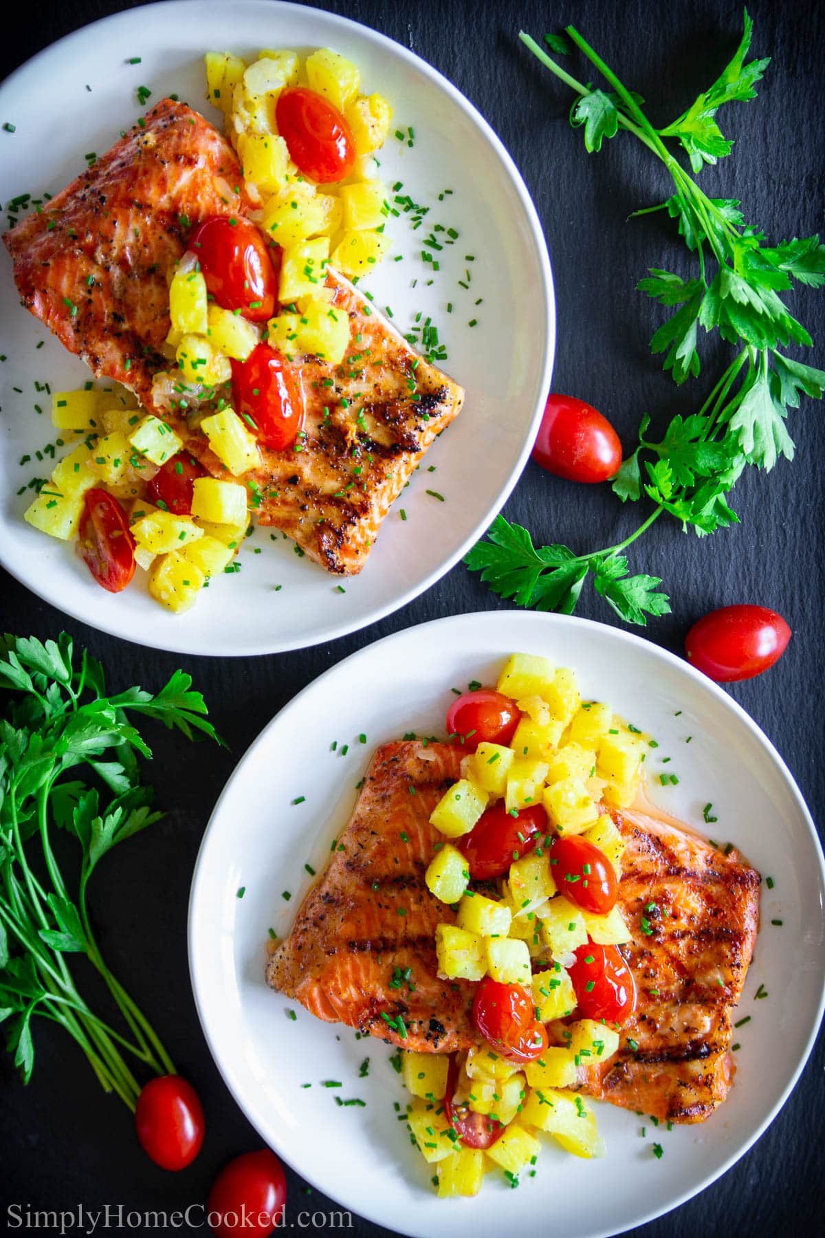 Pineapple Salmon on a plate with pineapple, cherry tomatoes, and chopped parsley on top.