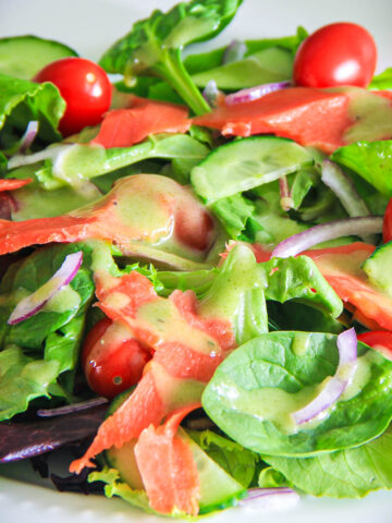 Close up of Smoked Salmon Salad with mixed greens, onion, cucumber, tomatoes, and dressing.