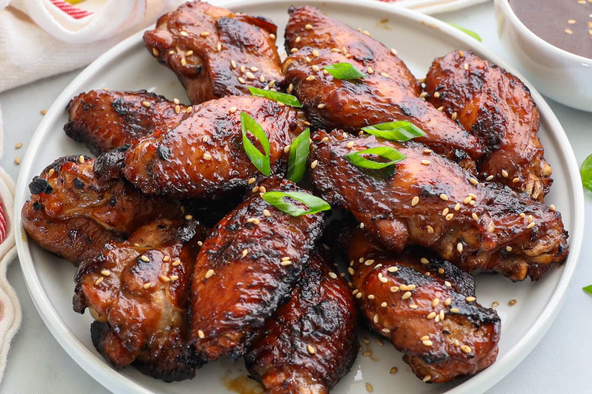 A plate of teriyaki chicken wings decorated with scallions and sesame.