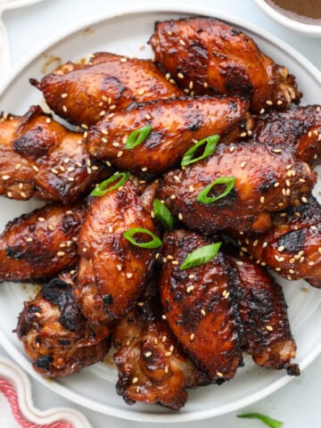 Teriyaki Chicken Wings garnished with sesame seeds and green onion on a white plate.