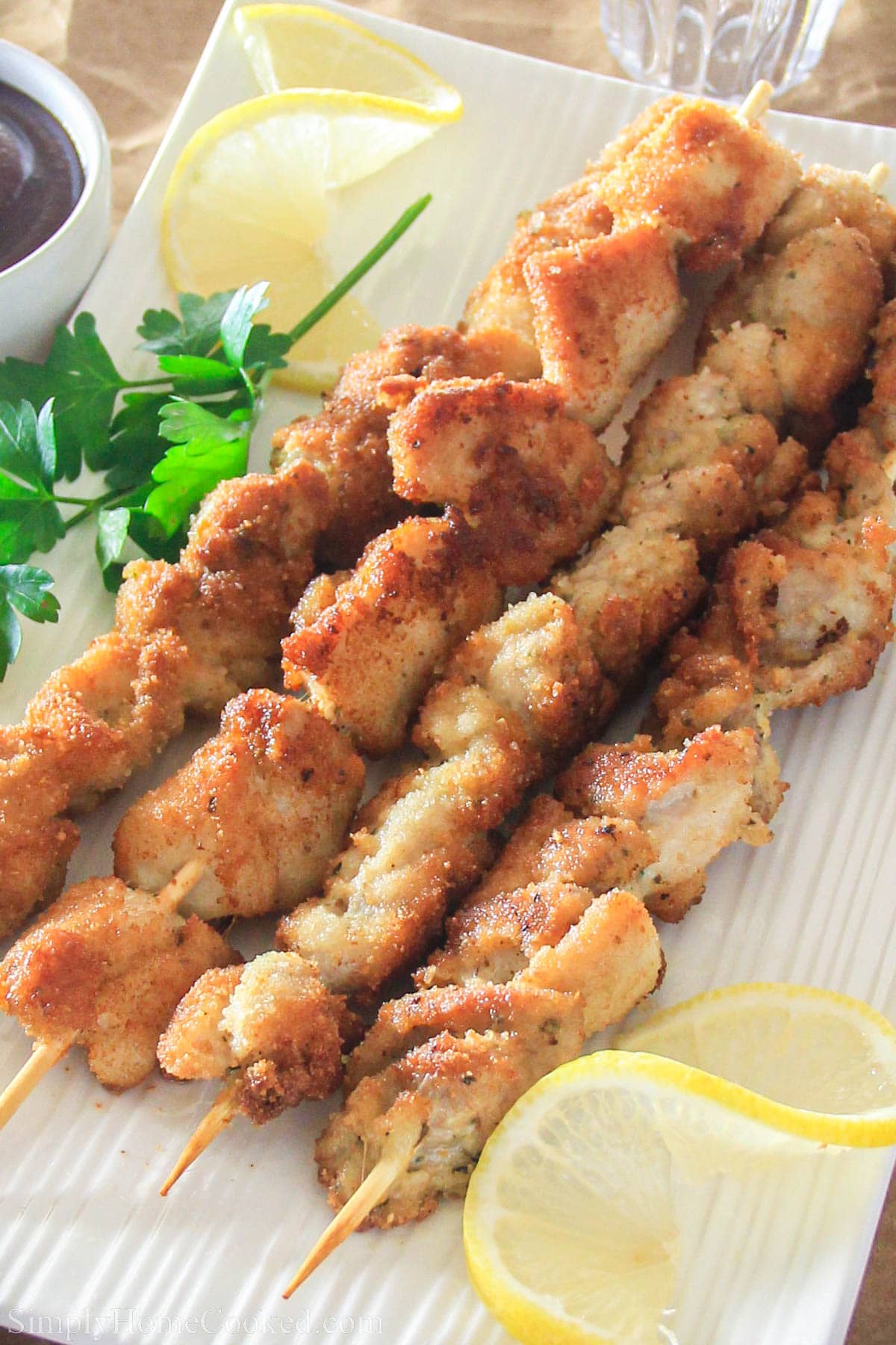 Breaded Chicken Skewers on a plate with lemon and parsley.