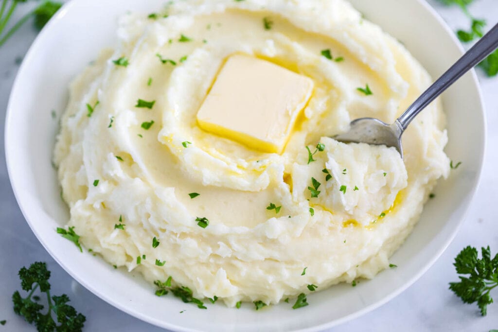 Super Creamy Mashed Potatoes in a bowl with butter and a spoon.