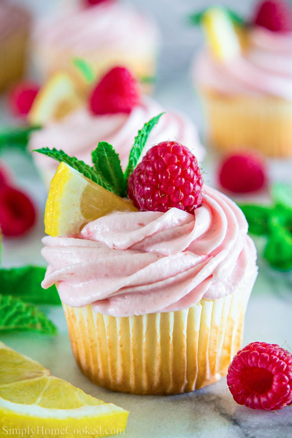 Lemon Raspberry Cupcake topped with lemon, mint, and a raspberry with more nearby.