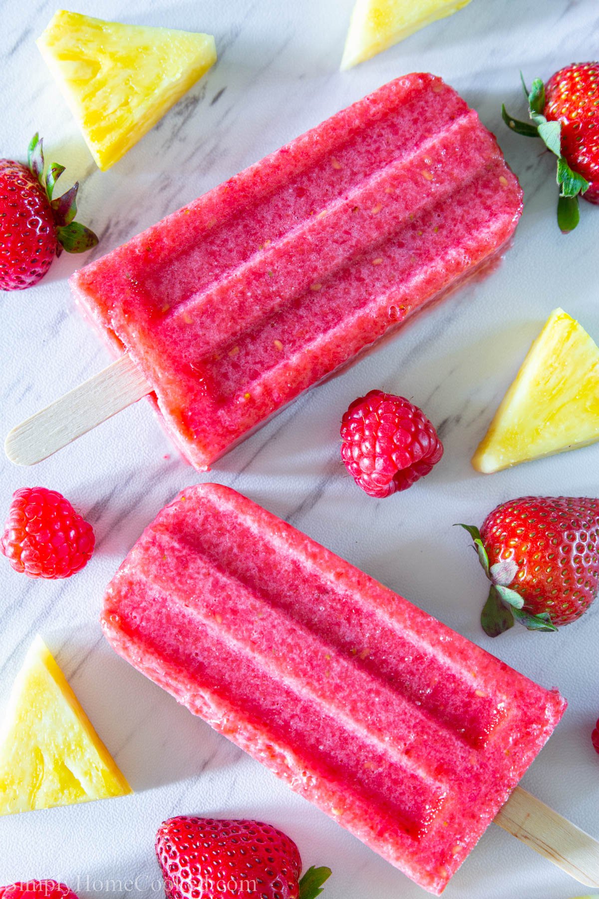 Strawberry Popsicles surrounded by pineapple chunks, strawberries, and raspberries.