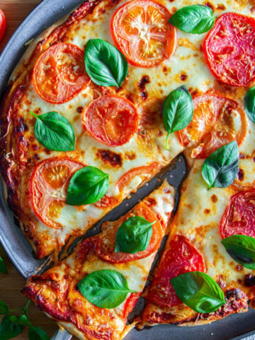 Margherita Pizza topped with tomatoes and basil with a piece cut out.