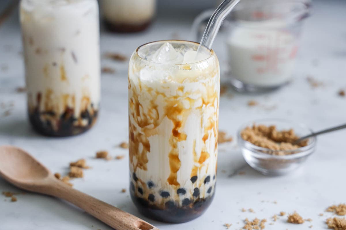 Brown Sugar Boba in a glass with a wooden spoon, milk, and brown sugar nearby.