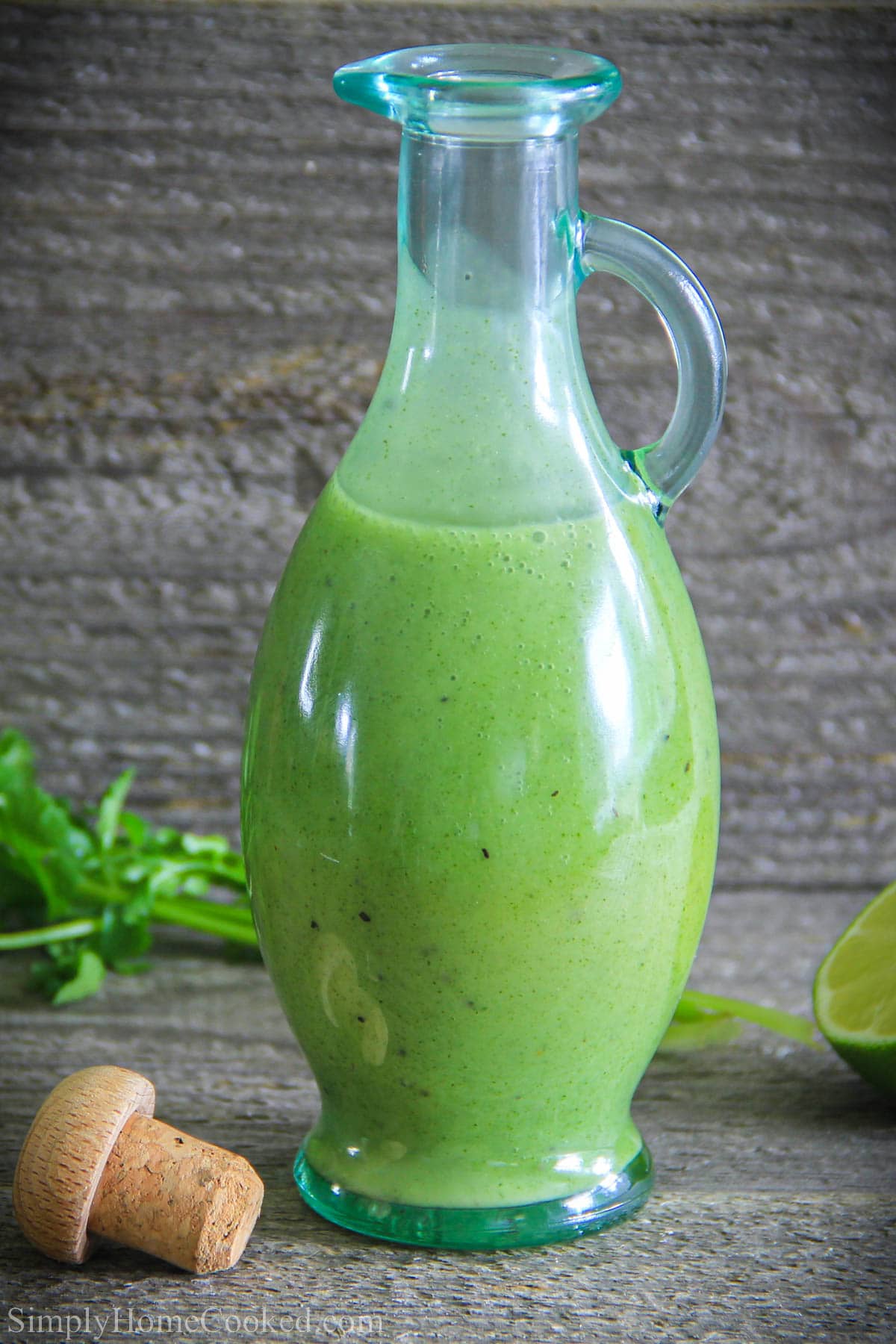 Cilantro Lime dressing in a carafe with a stopper, lime, and cilantro in the background