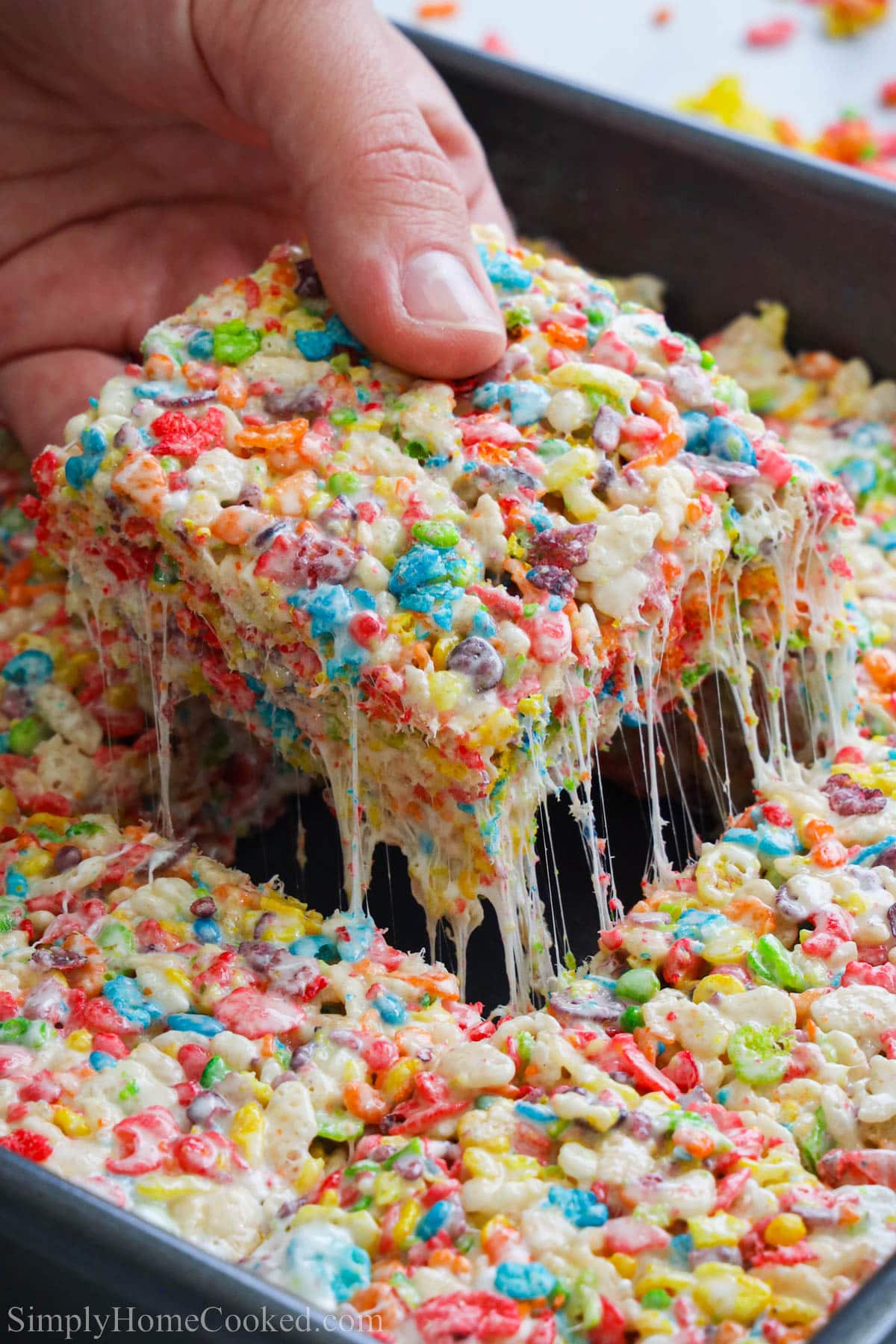 Fruity Pebbles Treats in a pan with one square being lifted out.