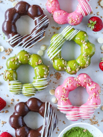 Mochi Donuts covered in matcha glaze, Nutella glaze, and strawberry glaze, then drizzled with white chocolate.