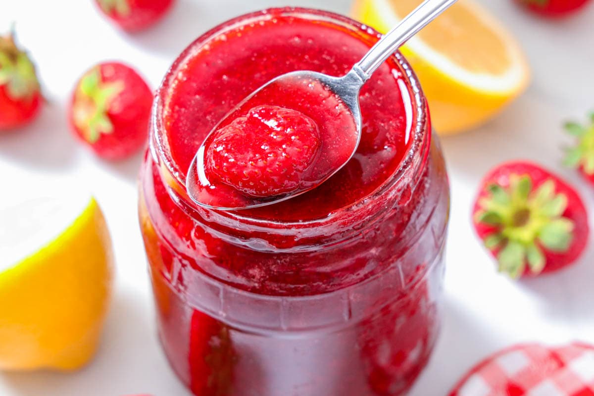 Overview of a jar of 3-ingredient Strawberry Jam with lemons and strawberries nearby.