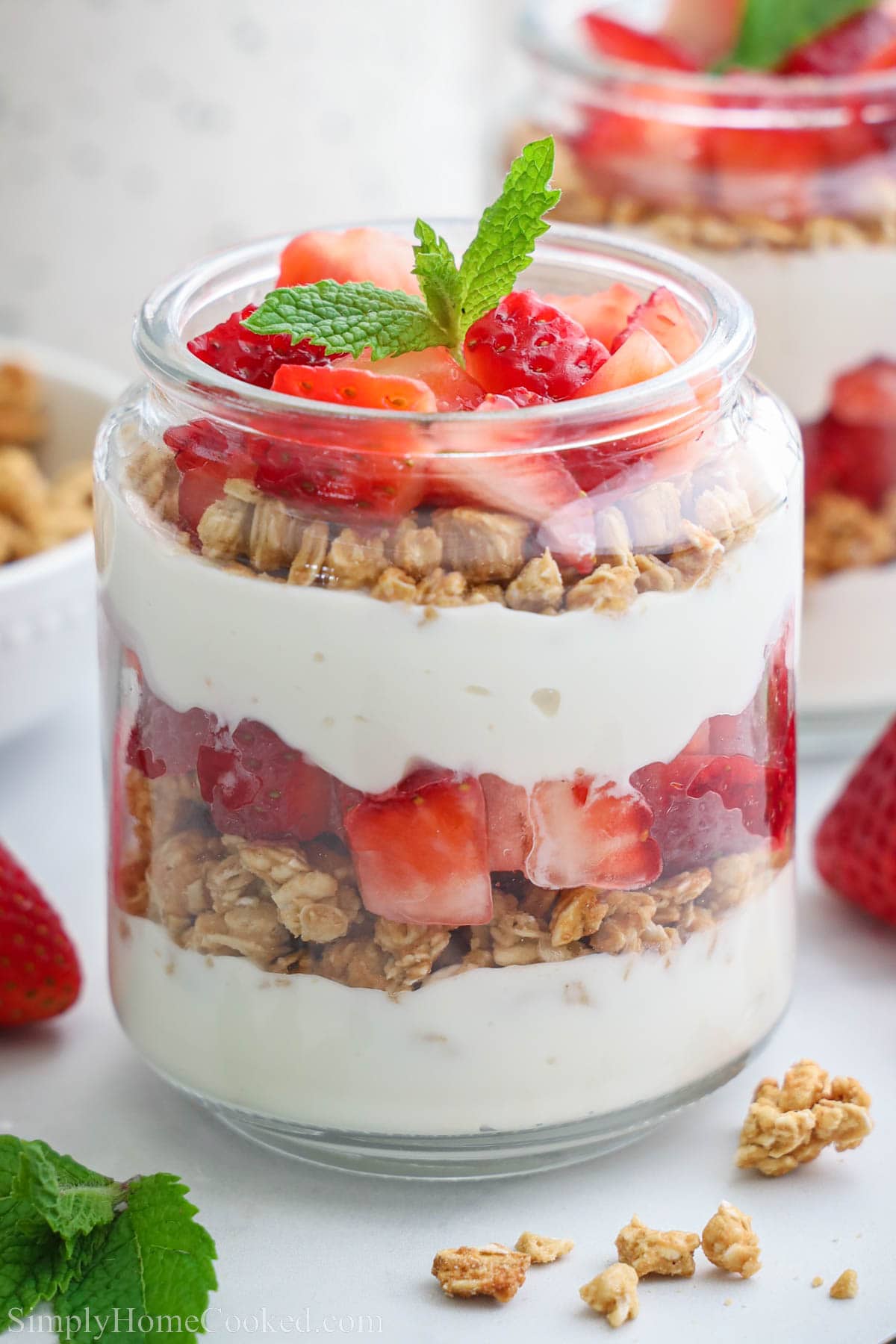 Strawberry parfait in a glass, layered with yoghurt, granola and strawberry pieces and garnished with a mint leaf.