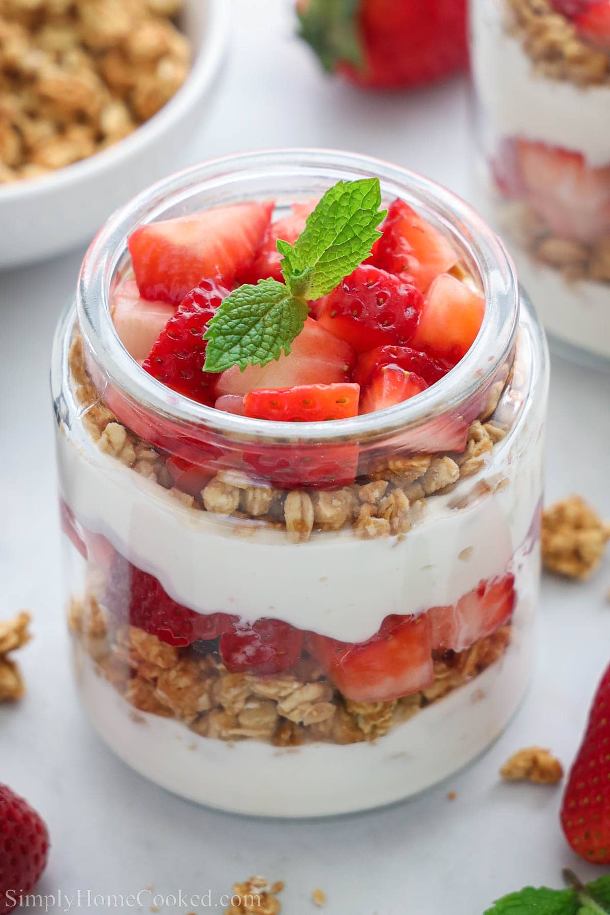 Strawberry parfait in a glass with muesli, honey and strawberries and garnished with mint.