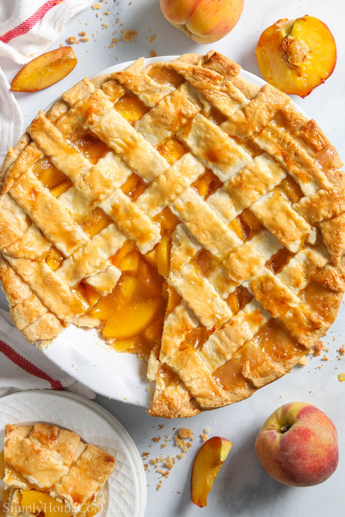 Perfect Peach Pie missing a piece surrounded by fresh peaches. 