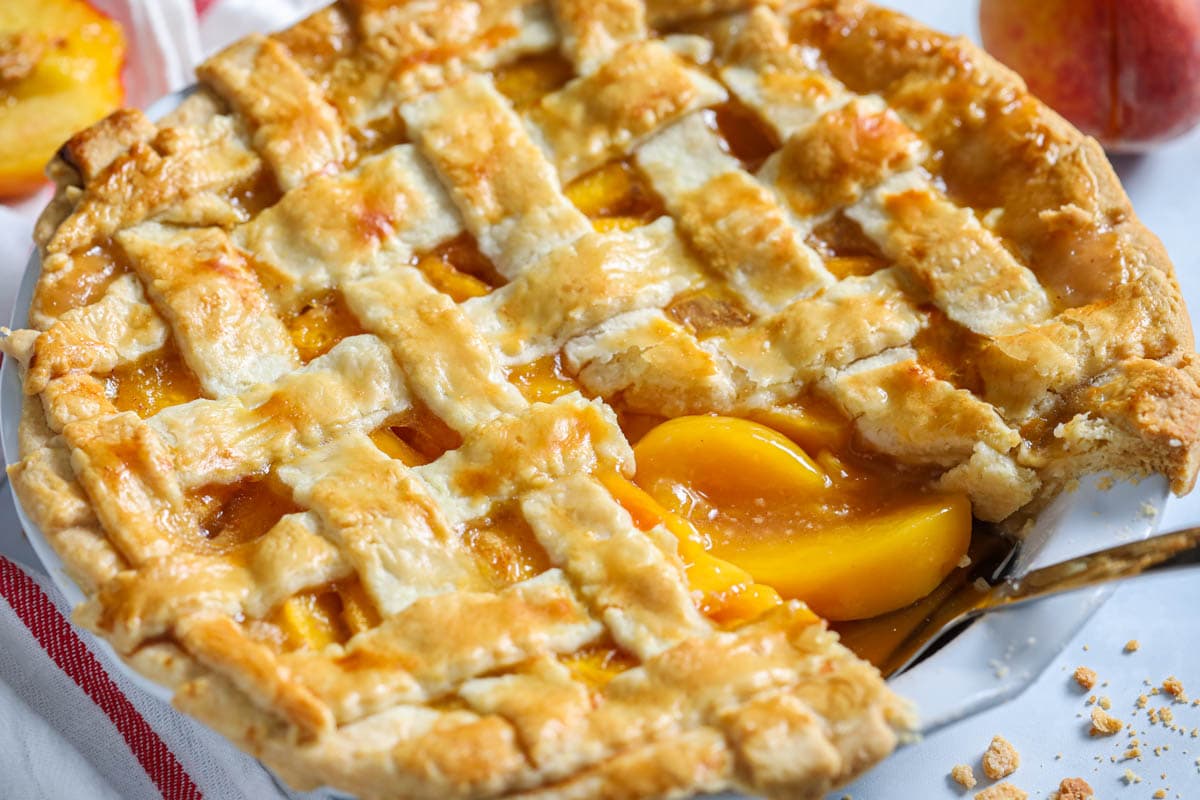 Perfect Peach Pie with a slice missing and a cake server lifting peach slices out. 