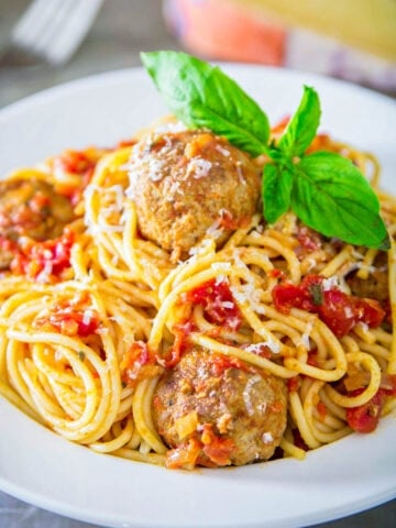 Spaghetti and Meatballs on a white plate topped with fresh basil.