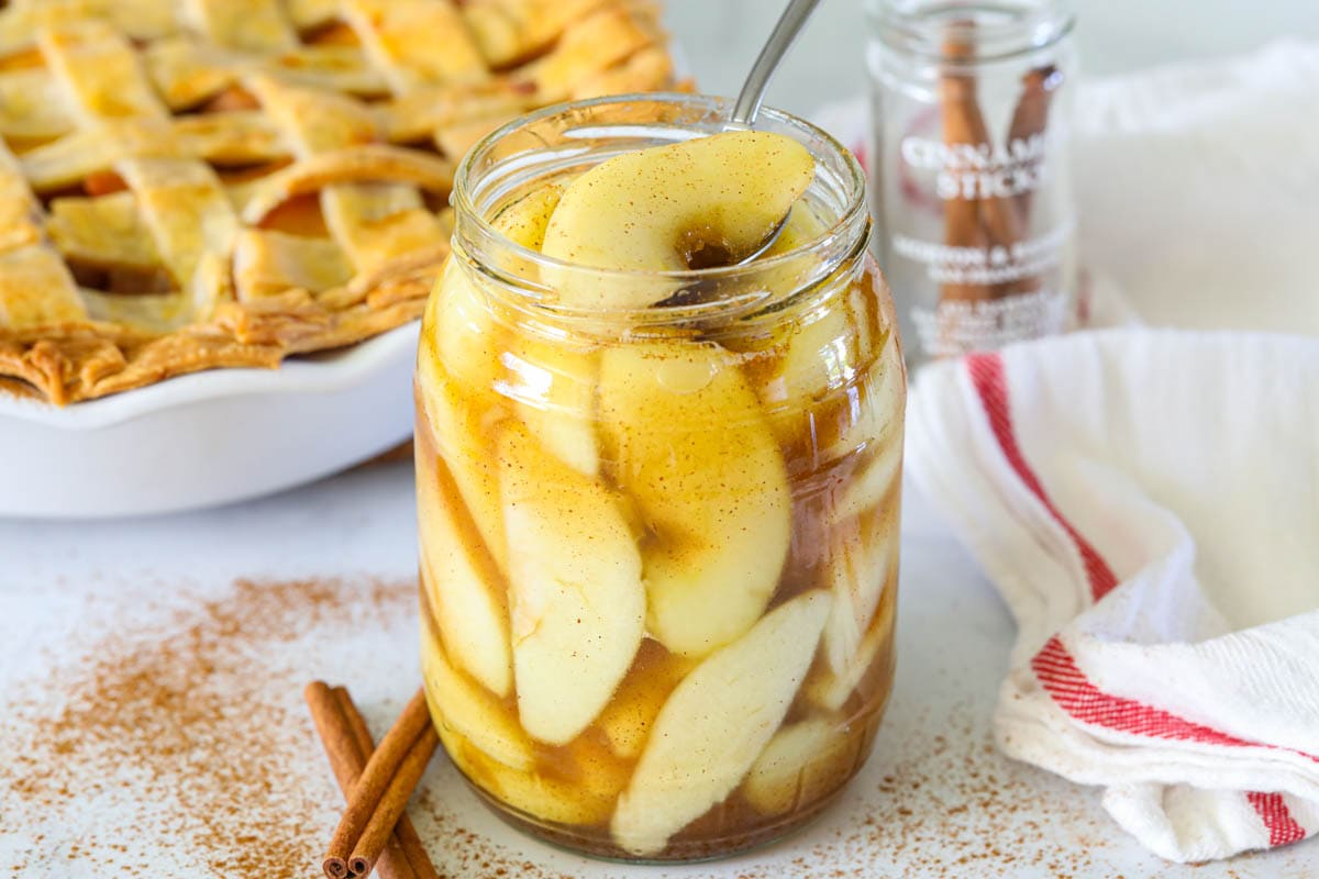 Homemade Apple Pie Filling in a mason jar with an apple pie in the background. 