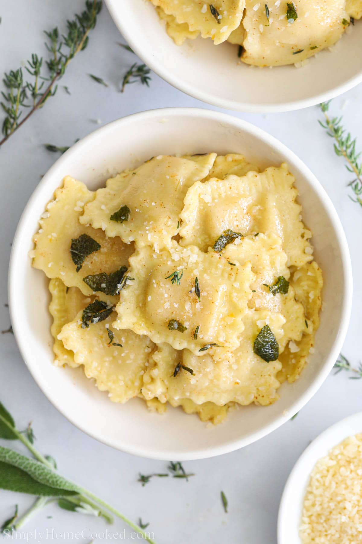 Butternut Squash Ravioli in a white bowl with fresh sage and thyme nearby.