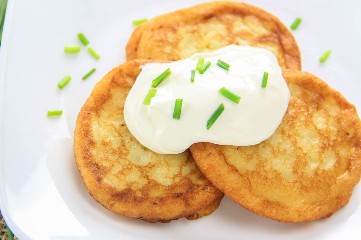 Mashed Potato Pancakes stacked and topped with sour cream and chives.