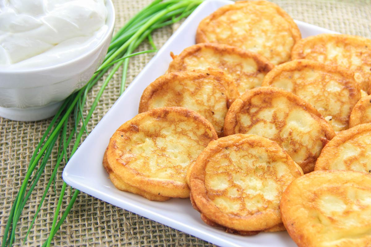 Mashed Potato Pancakes on a plate next to sour cream and chives.